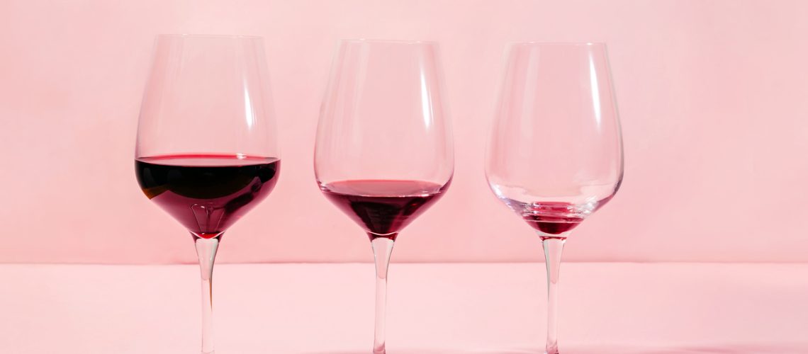 Mindful drinking and alcohol cutback concept. Three glasses with lowering levels of red wine poured, isolated on pink background