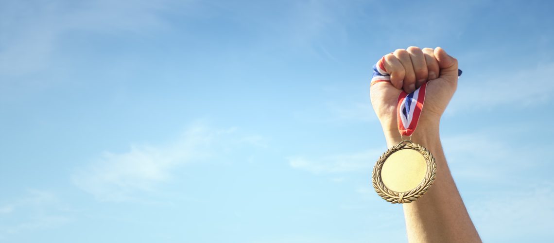 Gold medal winner held in athlete hand raised against blue sky background concept for winning, success and victory