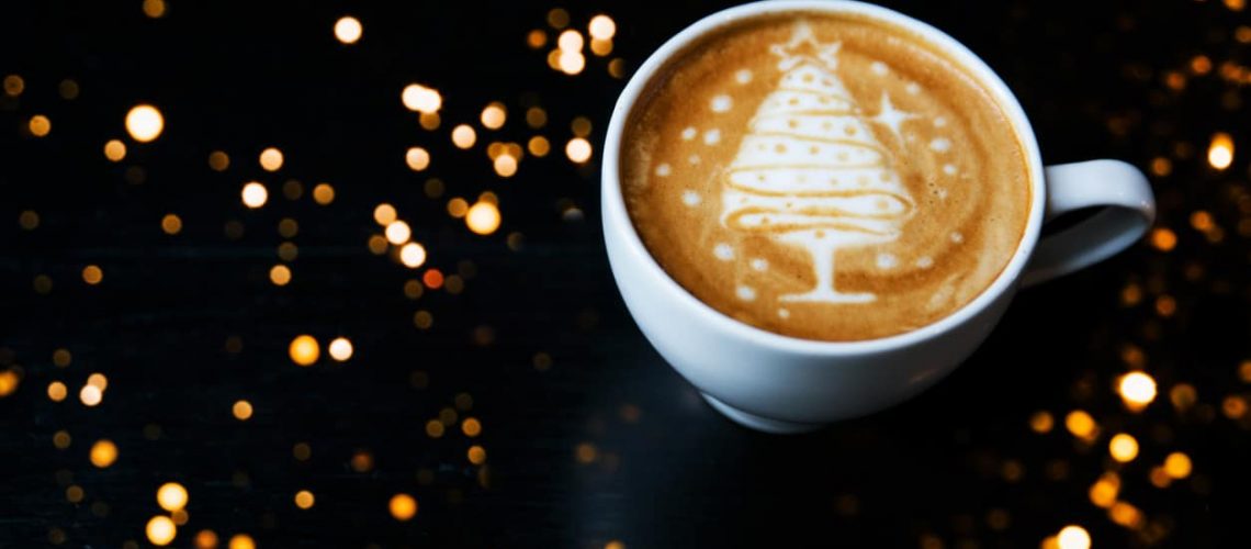Tasty cappuccino with Christmas tree latte art with some blurred lights. Holiday concept.