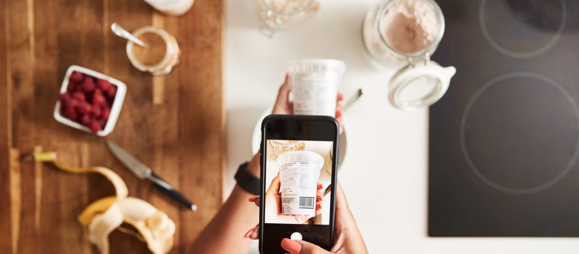 Woman Wearing Fitness Clothing Scanning QR Code On Food Packaging To Find Nutritional Information