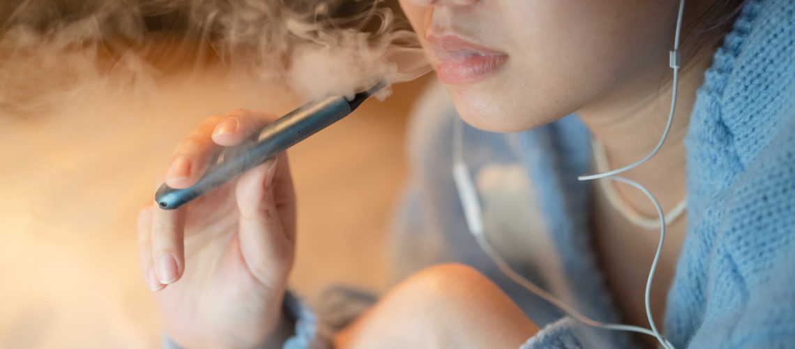 Young woman vaping an electronic cigarette for relax while working at night