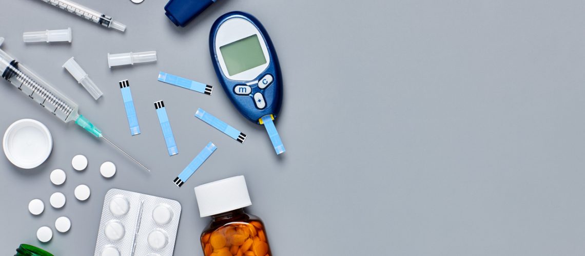 Directly above flat lay flat lay shot of medical equipment on gray background with copy space. Glucometer and stripes are placed with medicines and syringes. Blank space can be used for advertisement purpose.