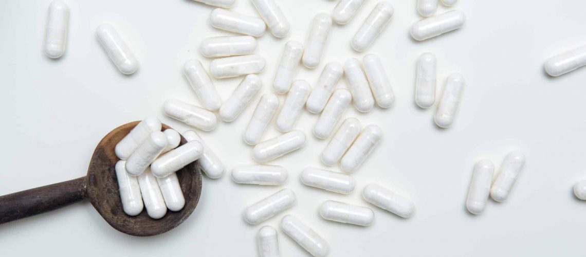 White tablets on a medicine dose spoon, with tablets across the table