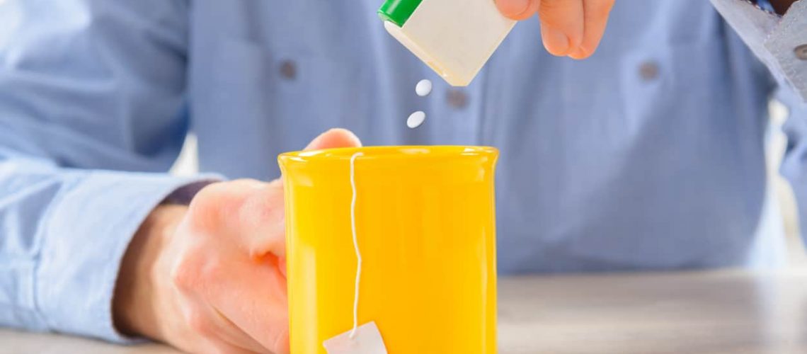 Sweetener tablets and hand with box whit cup of tea